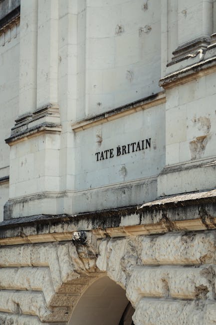 Close-up view of a section of a historic building with light-colored stone masonry, showing ornate architectural detailing including columns and decorative elements. Mounted on the façade is a metal 